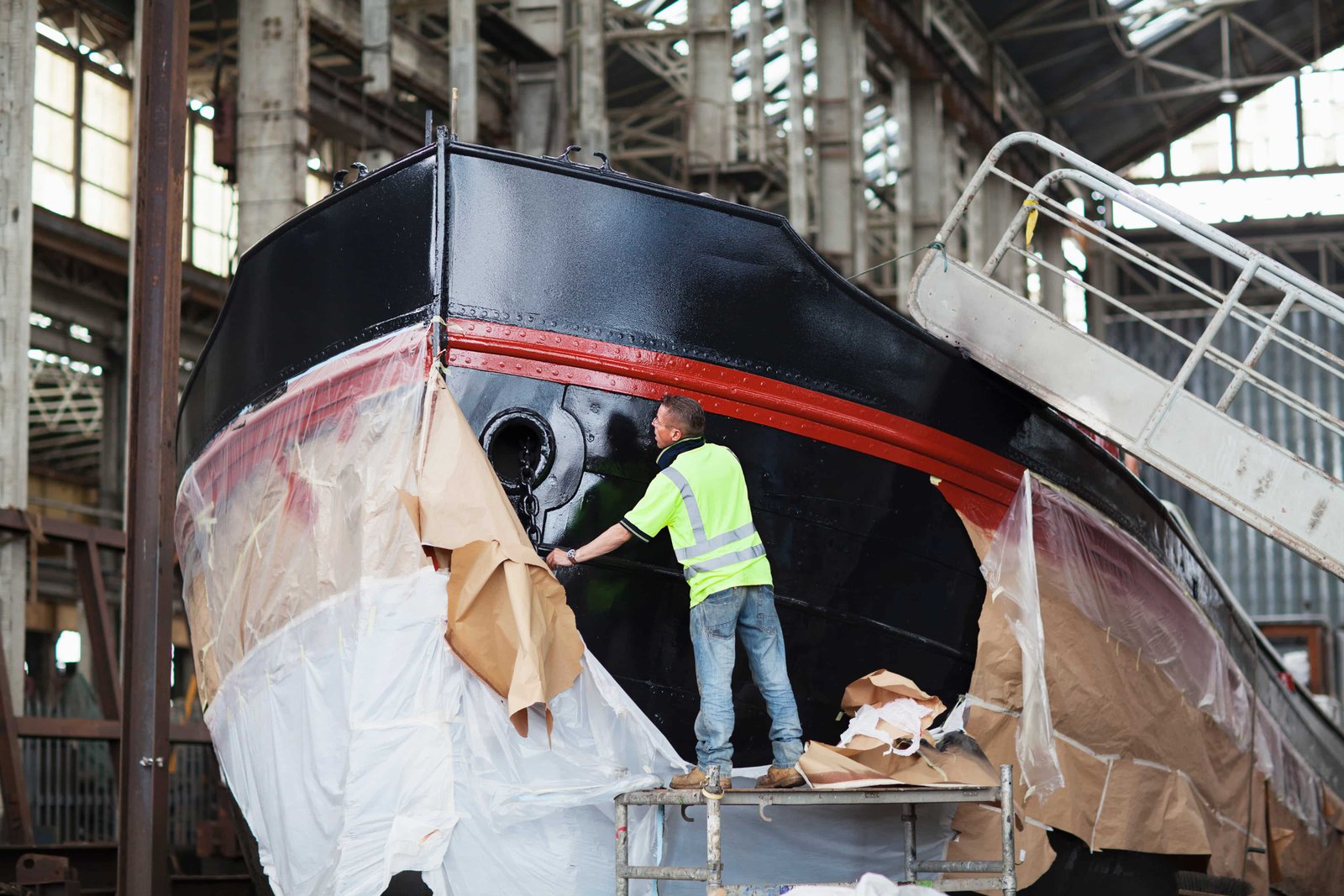 worker on top of scaffolding painting boat in shipyard